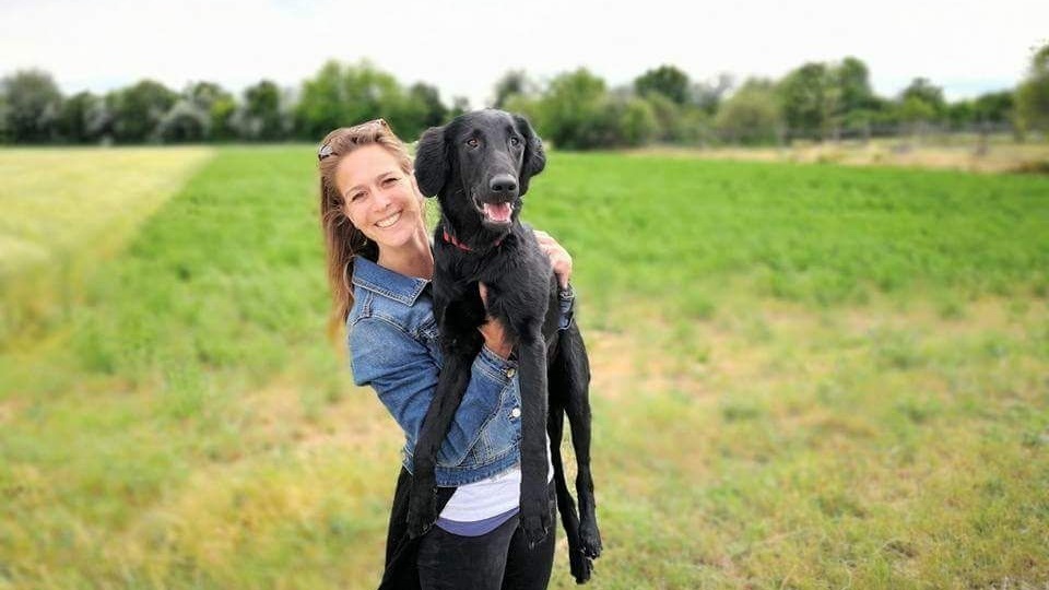 Rehahunde-Schule Besitzerin hält fröhlich eine schwarze Labrador Hundin Peppa auf den Händen